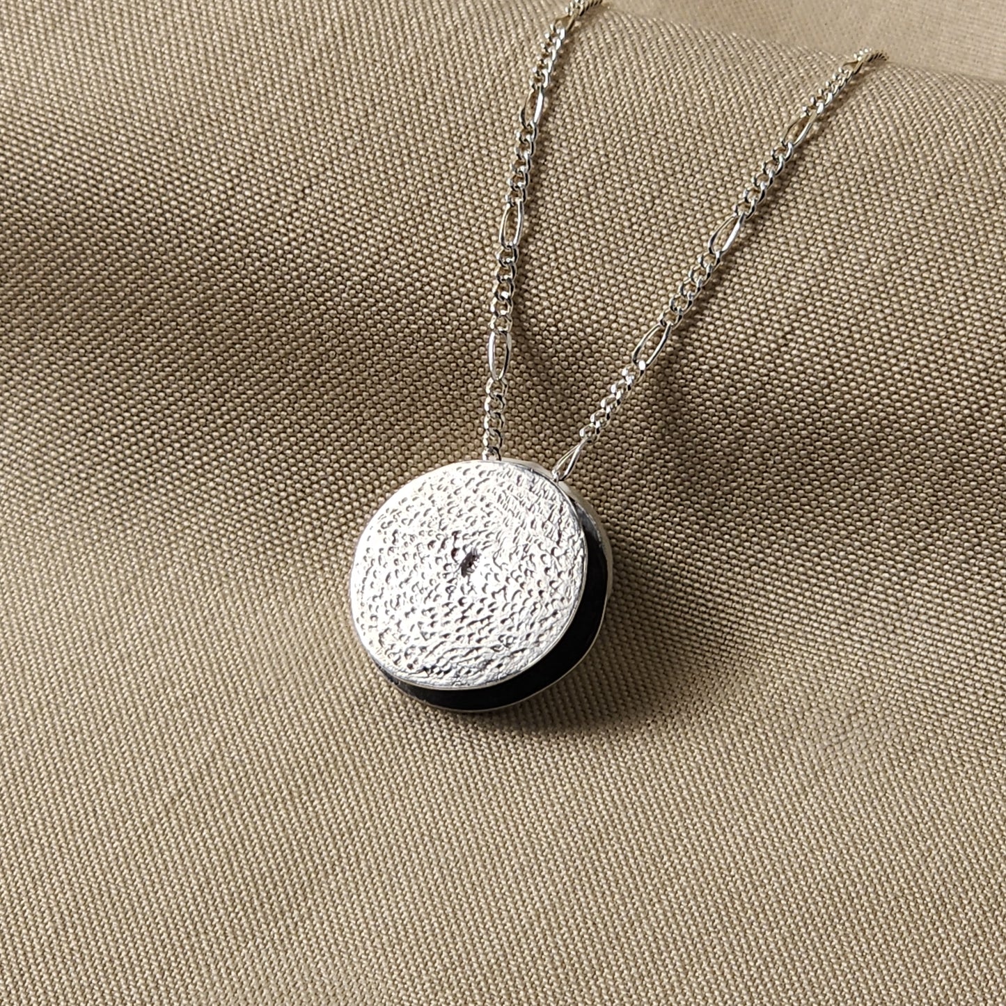 Silver necklace with a round pendant on a beige fabric background