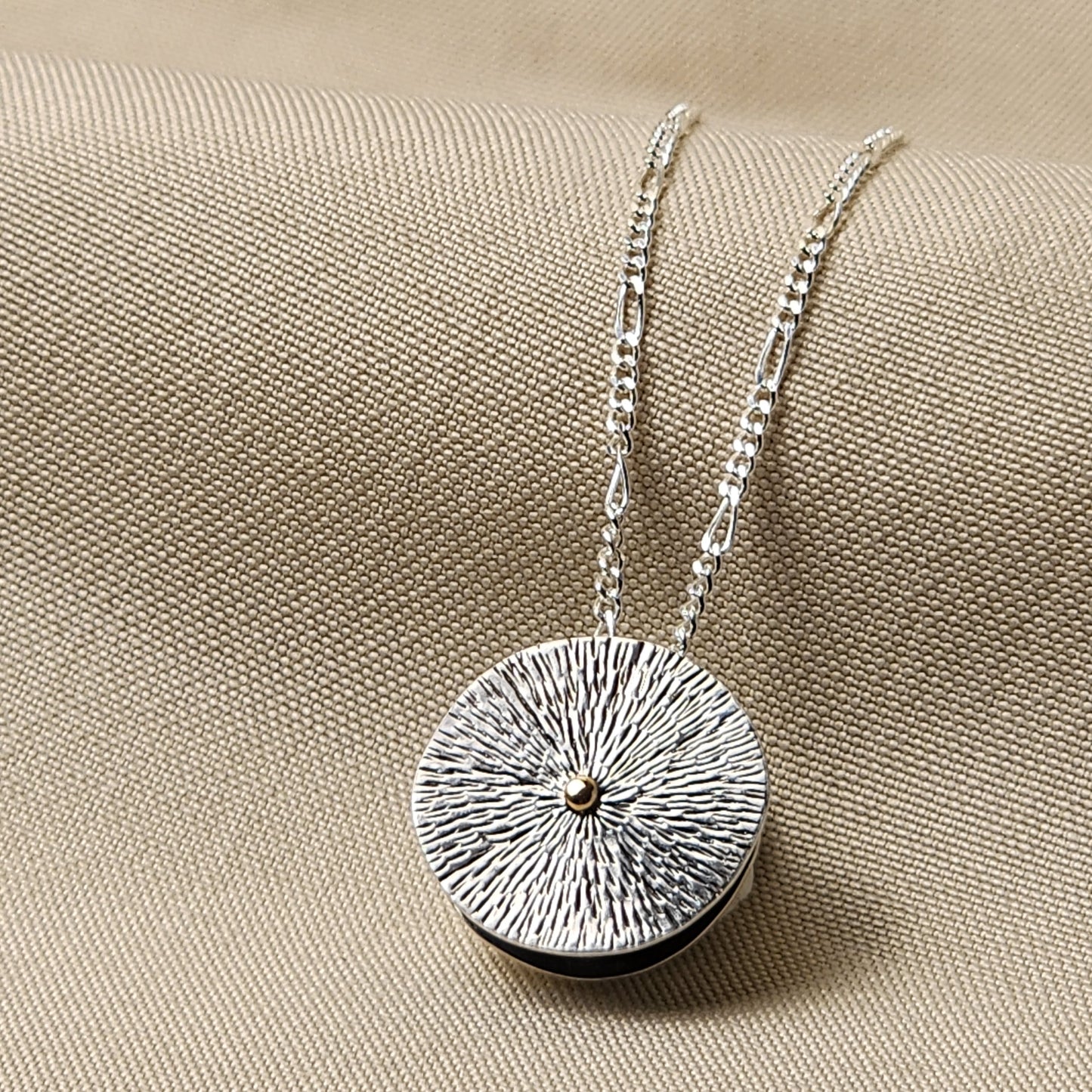 Silver necklace with a round textured pendant on a beige fabric background