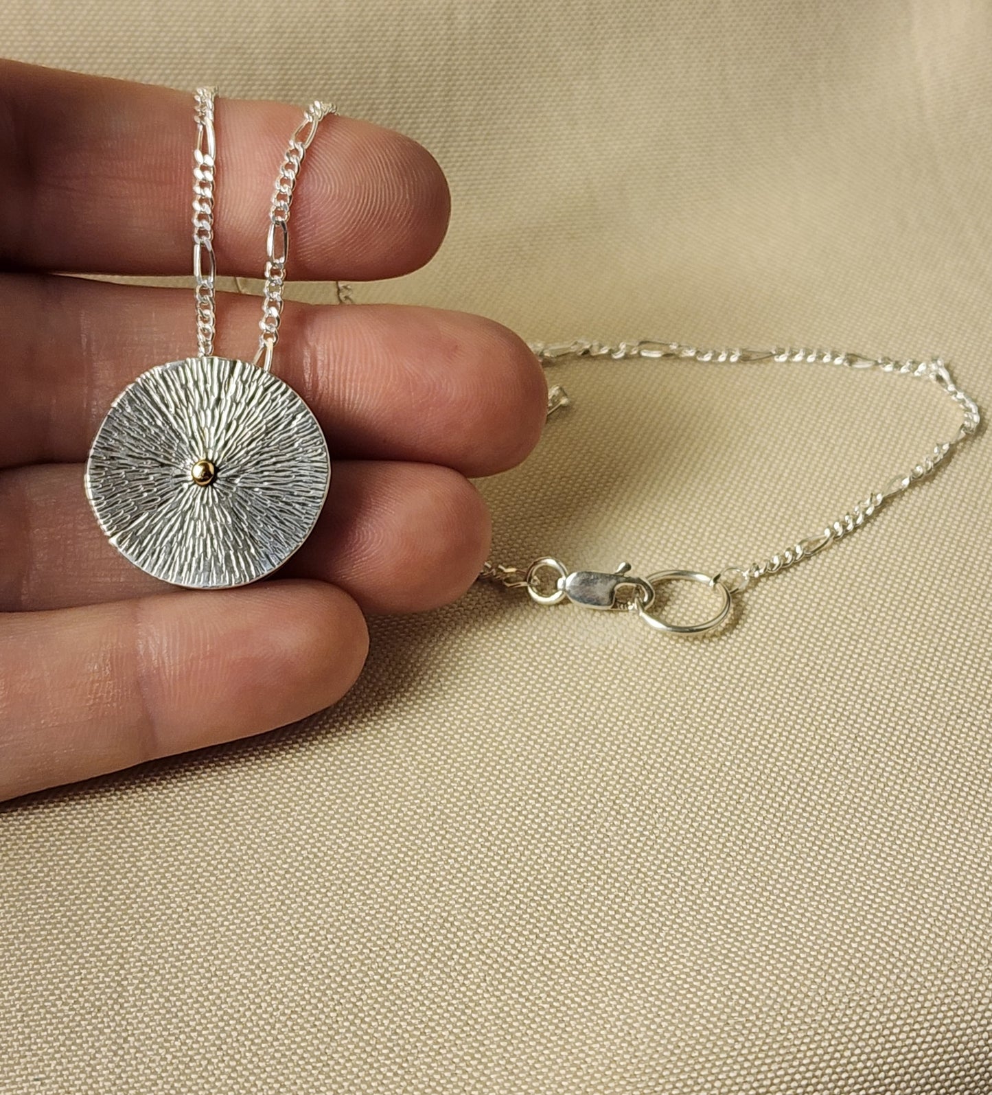 Silver necklace with a textured pendant held by a hand on a beige background